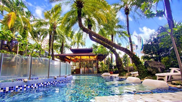 Una piscina cristalina con borde de azulejos, rodeada de palmeras y una zona de estar cubierta.