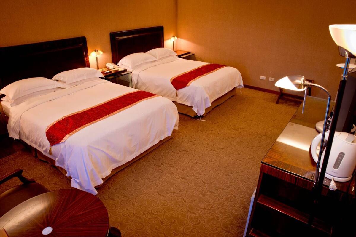 A hotel room with two beds, a desk with a lamp, and a massage chair.