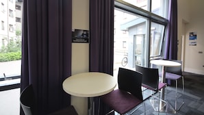 A modern indoor seating area with two round tables and chairs, large windows with curtains, and a visible outdoor view. - Edinburgh Metro Youth Hostel (Edinburgh)