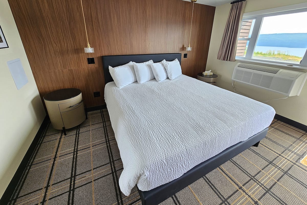 Hotelkamer met een groot bed, houten paneelwanden, een raam met uitzicht en een plafondventilator.
