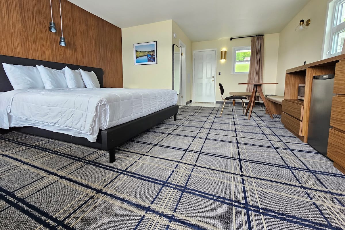 Een hotelkamer met een bed, een bureau, een stoel, een koelkast en een deur die naar een andere kamer leidt.