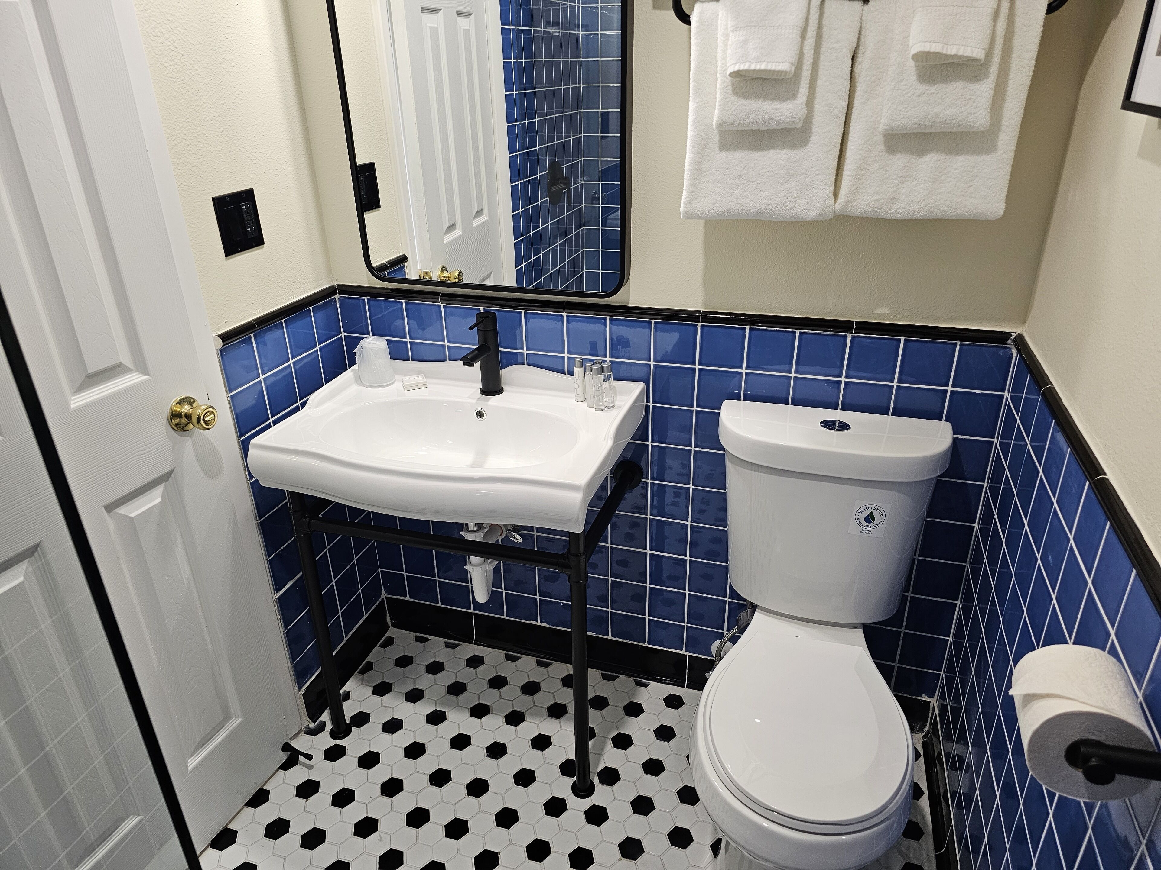 Ein Badezimmer mit weißem Waschbecken, schwarzen und weißen sechseckigen Bodenfliesen, einer weißen Toilette und blauen Wandfliesen.