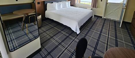 A hotel room with a large bed, a small table, a bench, and a view of a body of water through a window.