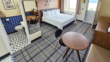 Habitación de hotel con cama, una mesa redonda, una silla, baño con inodoro y lavabo, y una ventana con cortinas.
