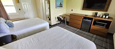 A hotel room with two beds, a desk, a chair, a television, and a kitchenette.