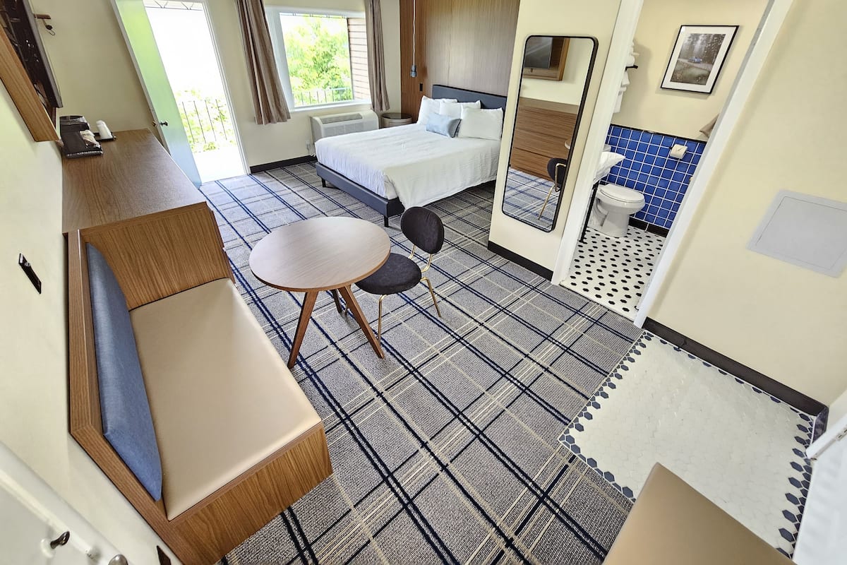 Hotelkamer met een bed, een kleine tafel met twee stoelen, een bank, een badkamer met toilet en wastafel, en een raam met gordijnen.