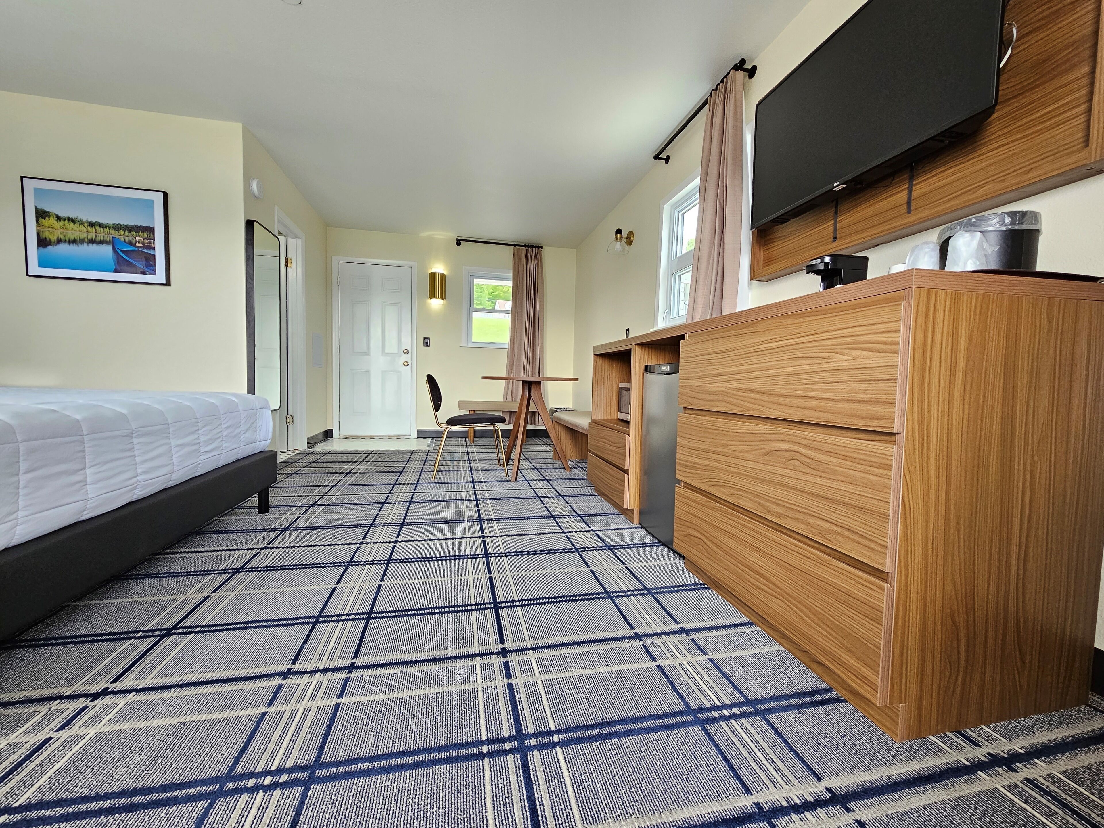 A hotel room with a bed, a wooden dresser, a television, and a view of a lake through the window.