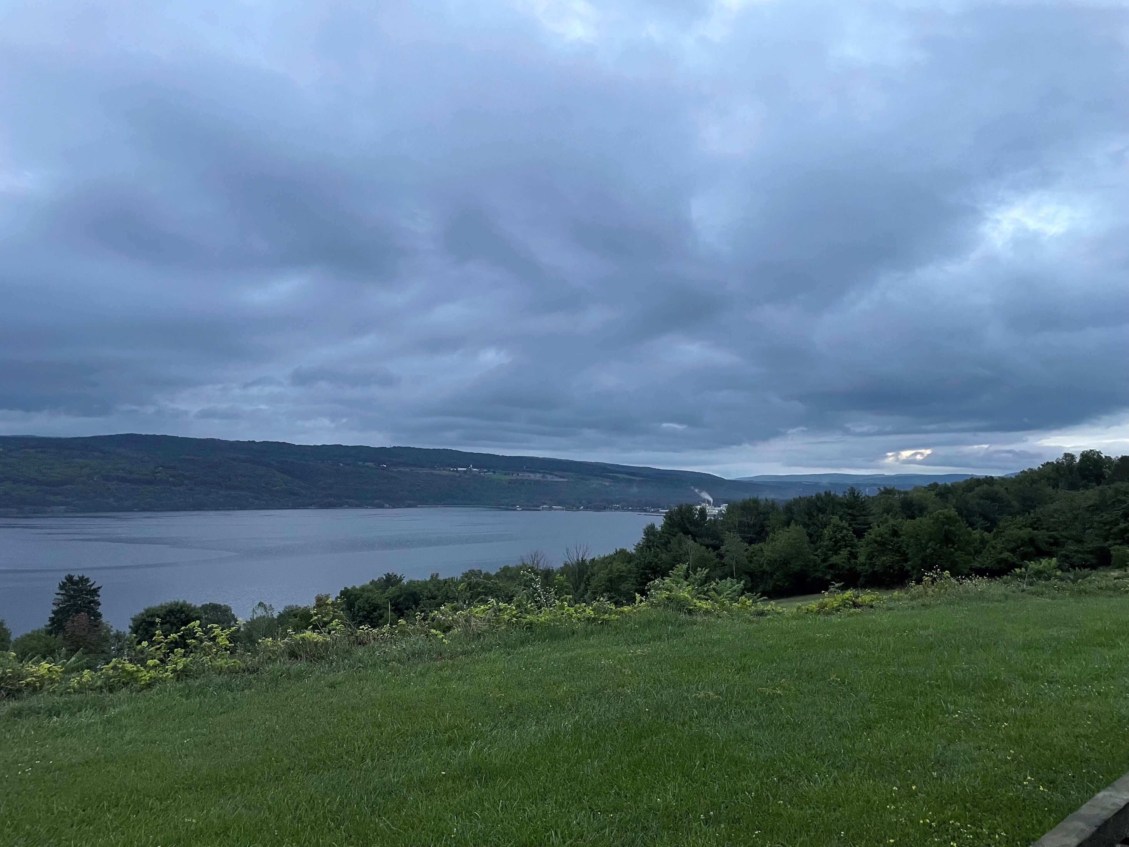 Une vue d’un lac, avec une étendue herbeuse au premier plan et des collines en arrière-plan.
