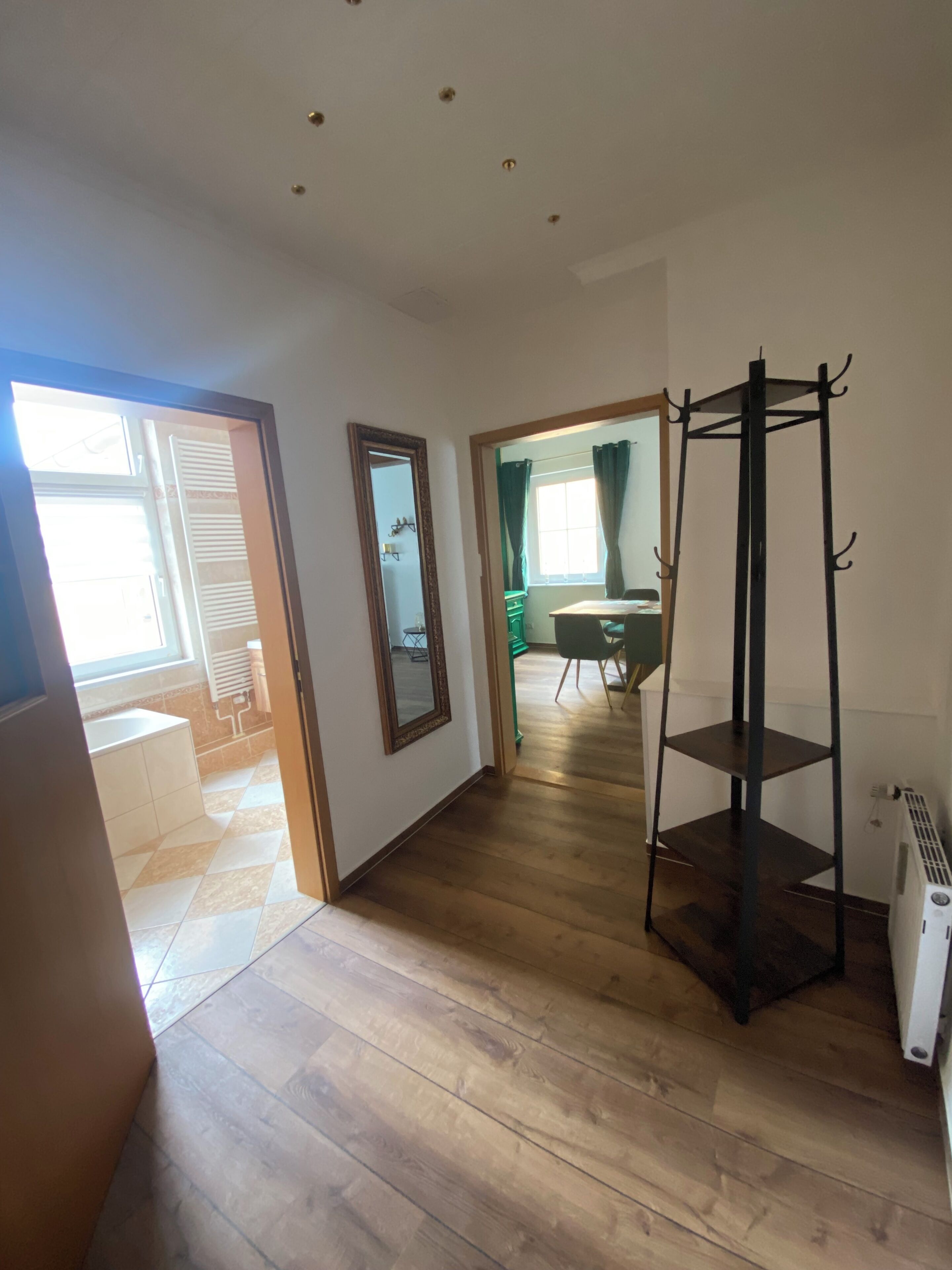 Quarto com piso de madeira, aquecedor portátil, espelho e janela com cortinas.