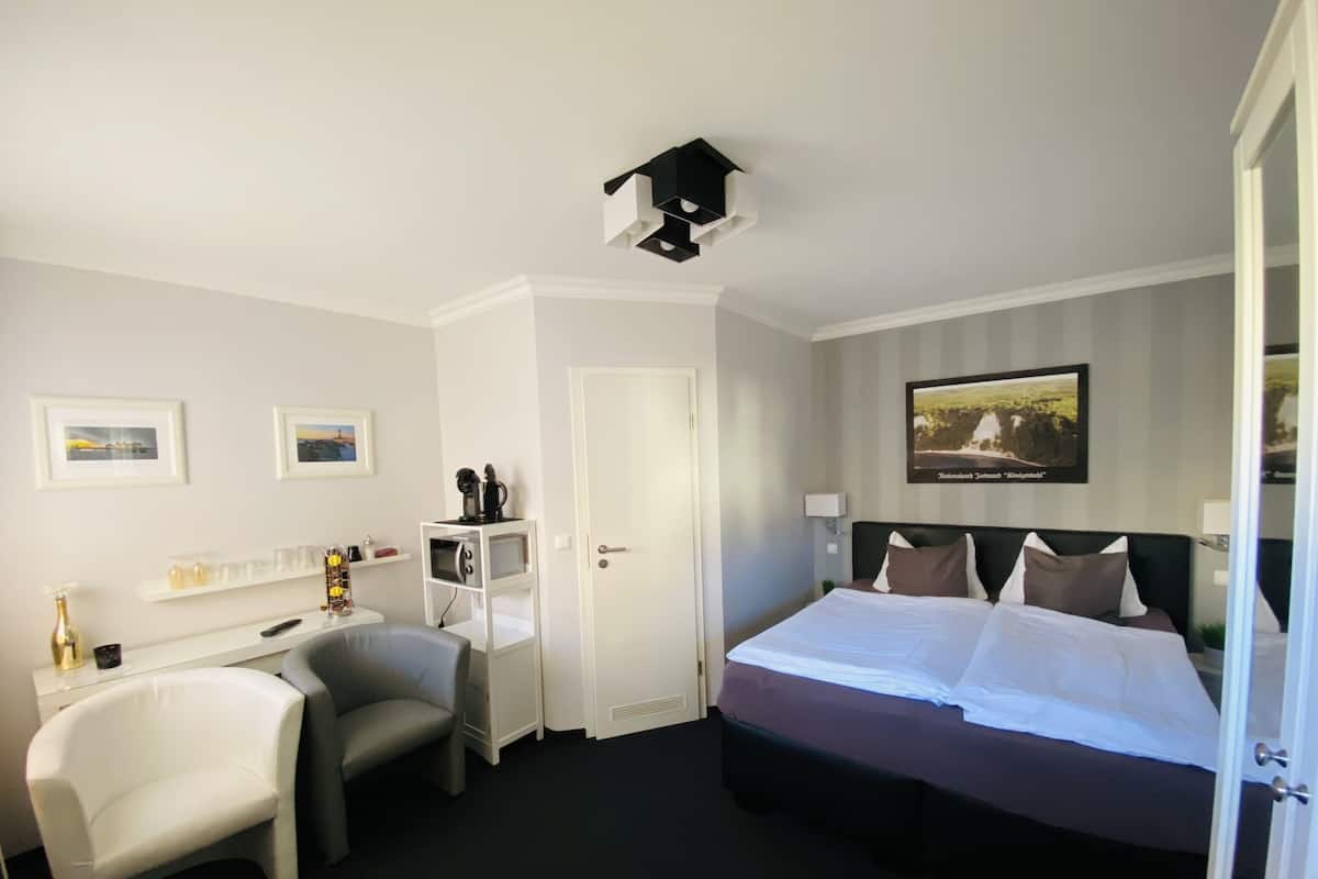 Une chambre d’hôtel comprenant un lit, un bureau avec une chaise, une machine à café et une petite étagère avec quelques objets.