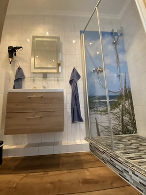 Un baño moderno con tocador de madera, cabina de ducha de vidrio y vista a un paisaje montañoso a través de la ducha.