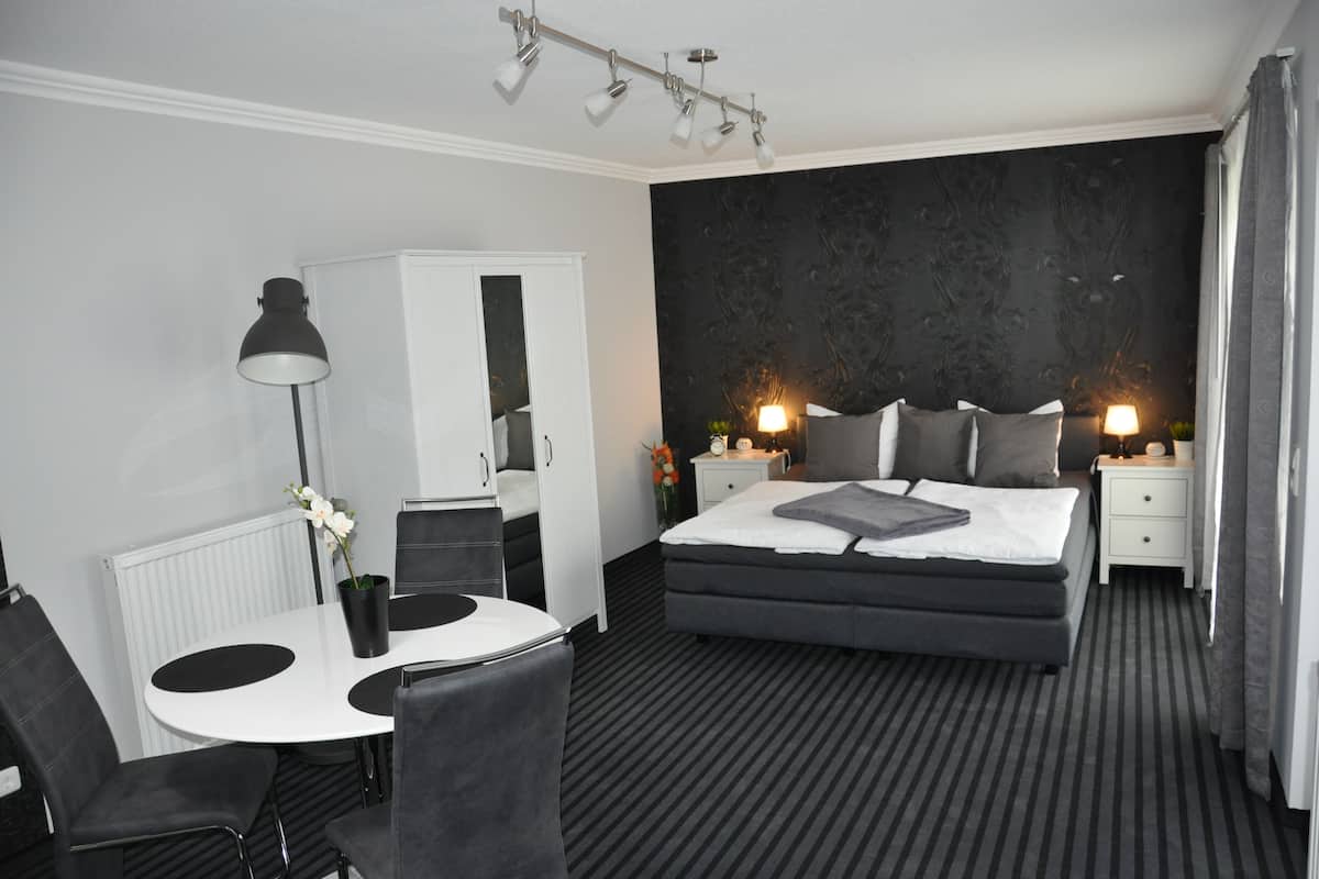 Une chambre d’hôtel moderne avec un grand lit, un bureau avec une chaise, un radiateur blanc et un mur à motifs sombres.
