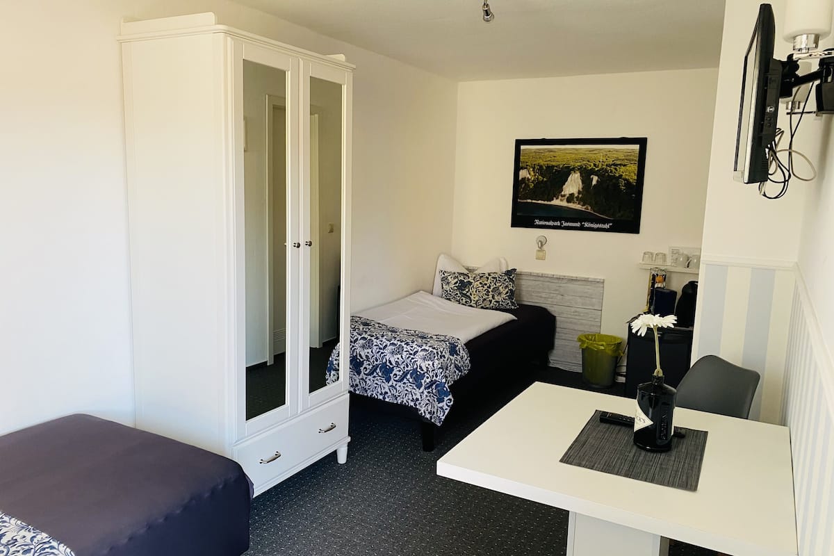 Une petite pièce propre et bien rangée, avec un lit, un bureau, une armoire et un tableau encadré au mur.