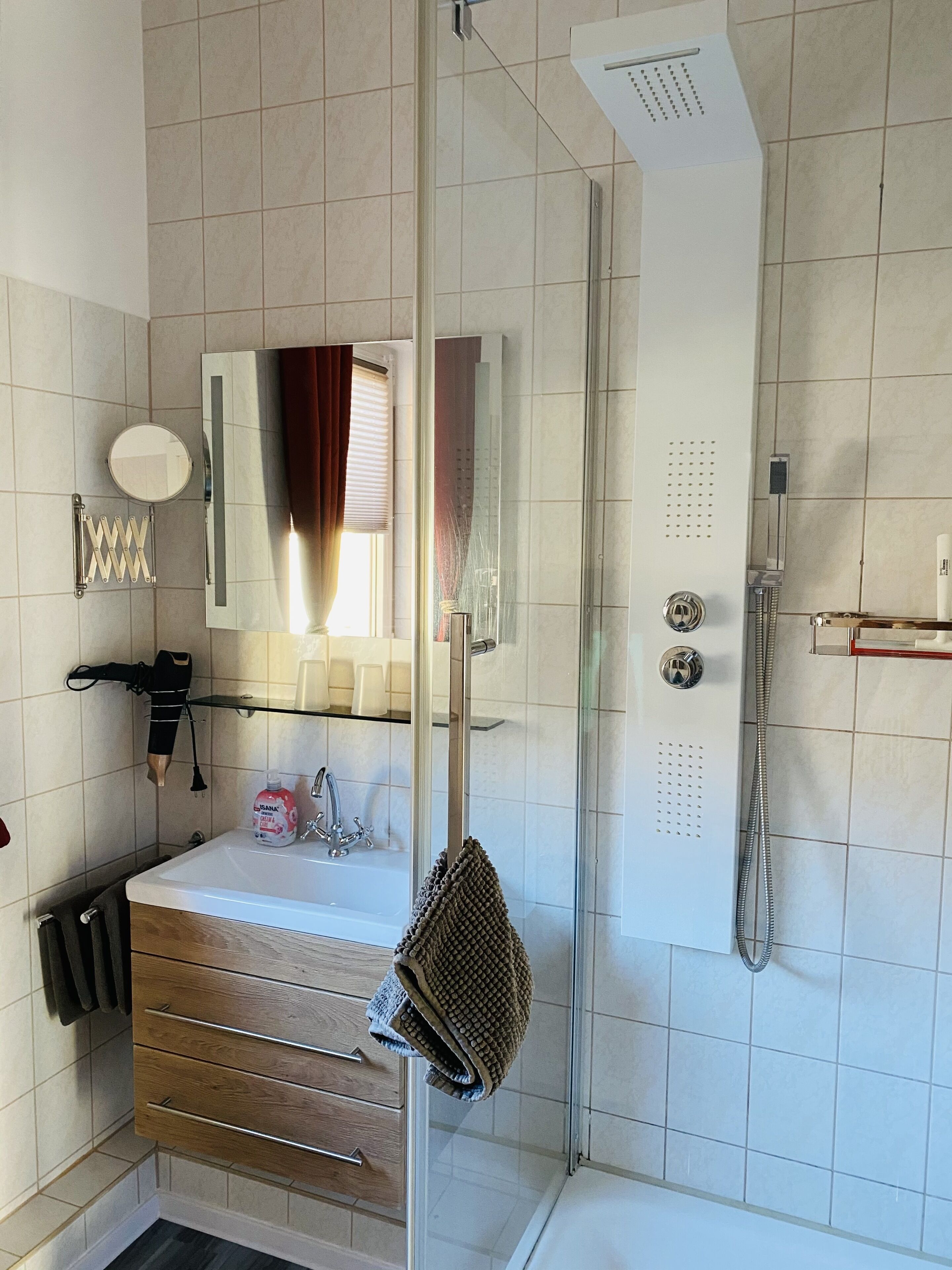 Ein Badezimmer mit einer Duschkabine, einem Waschbecken mit Spiegel darüber und einem Handtuchhalter.