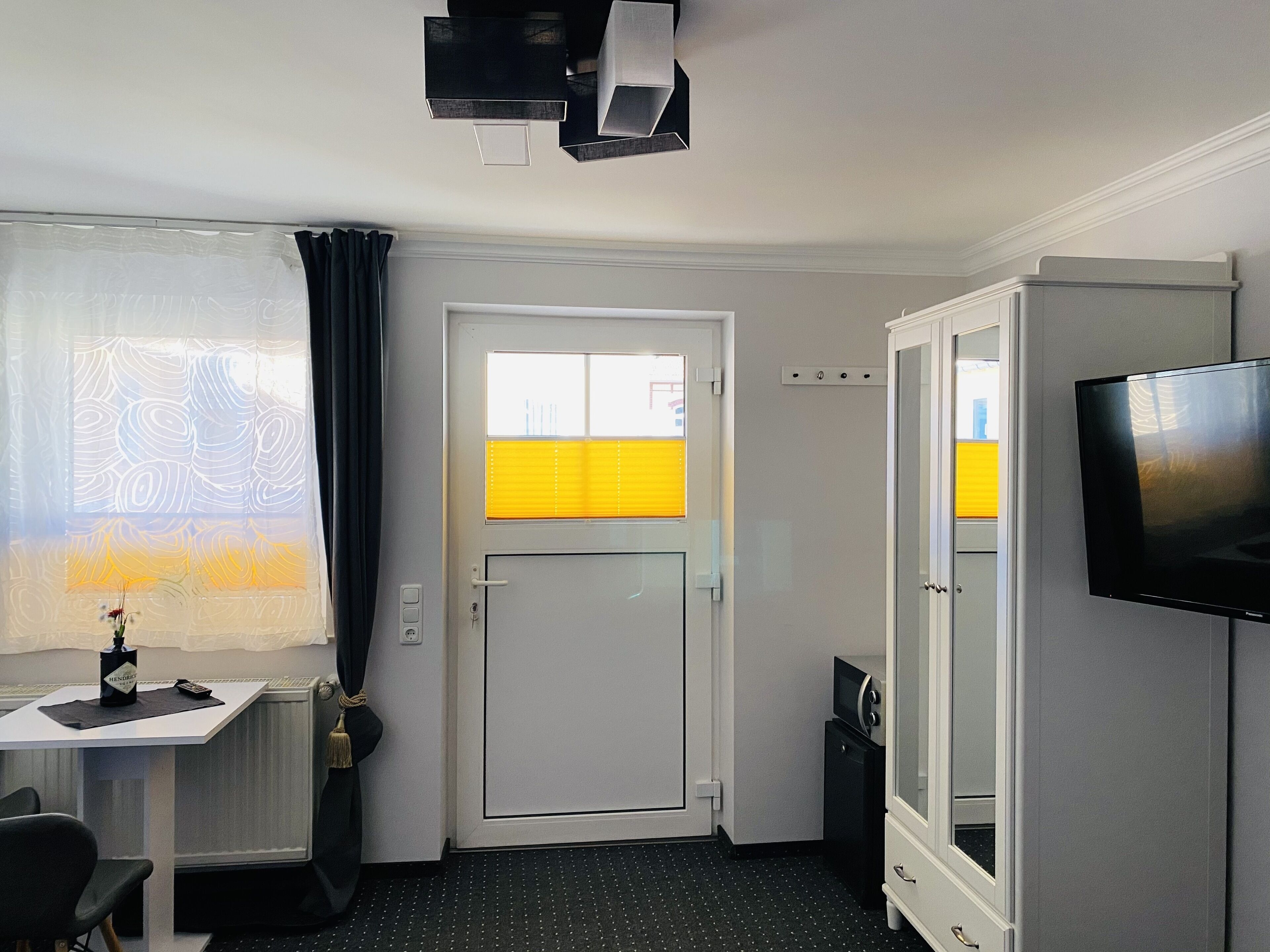 A hotel room with a desk, chair, television, wardrobe, and a door with a window.