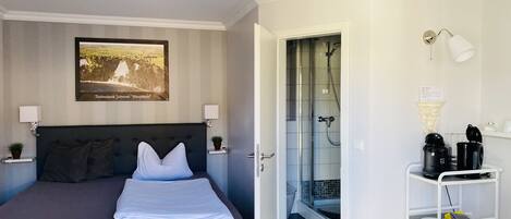 Una habitación de hotel con cama, ducha, una kitchenette pequeña y un cubo de basura.