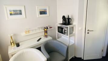 Una habitación pequeña y ordenada con un escritorio blanco, dos sillas, un microondas y una puerta.