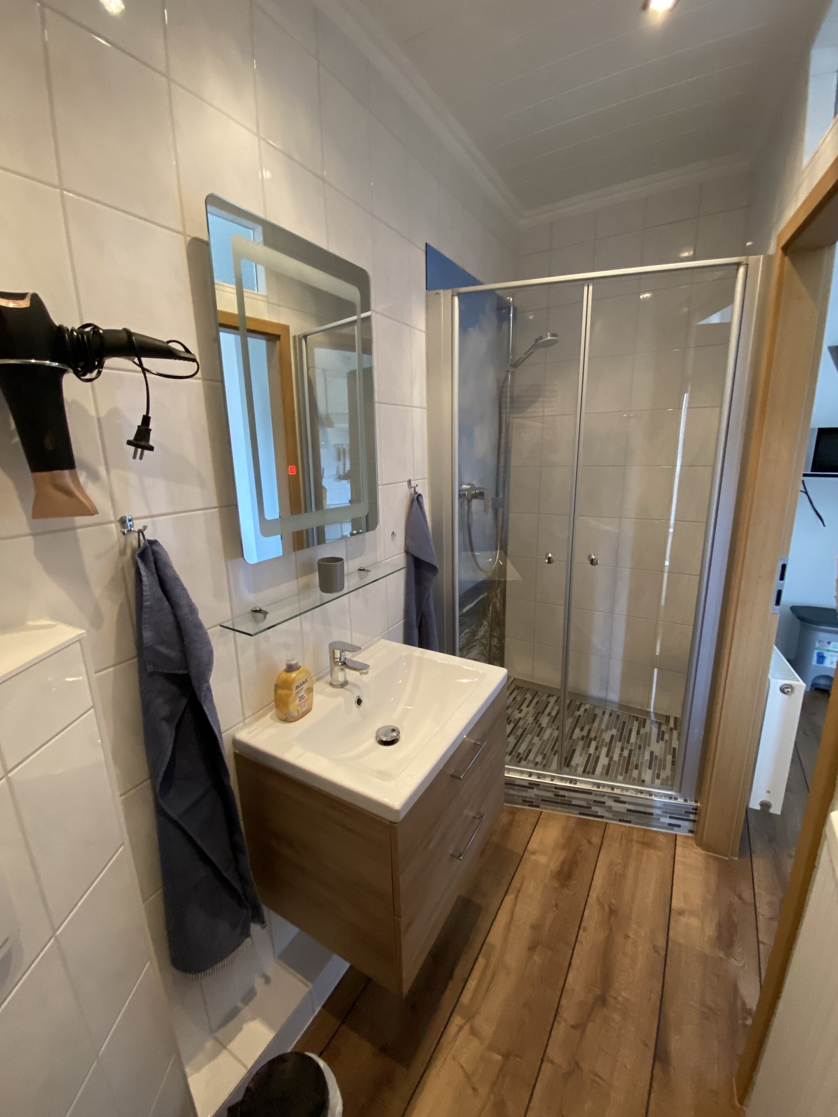 A modern bathroom with a glass-enclosed shower, a vanity with a mirror, and a towel rack.