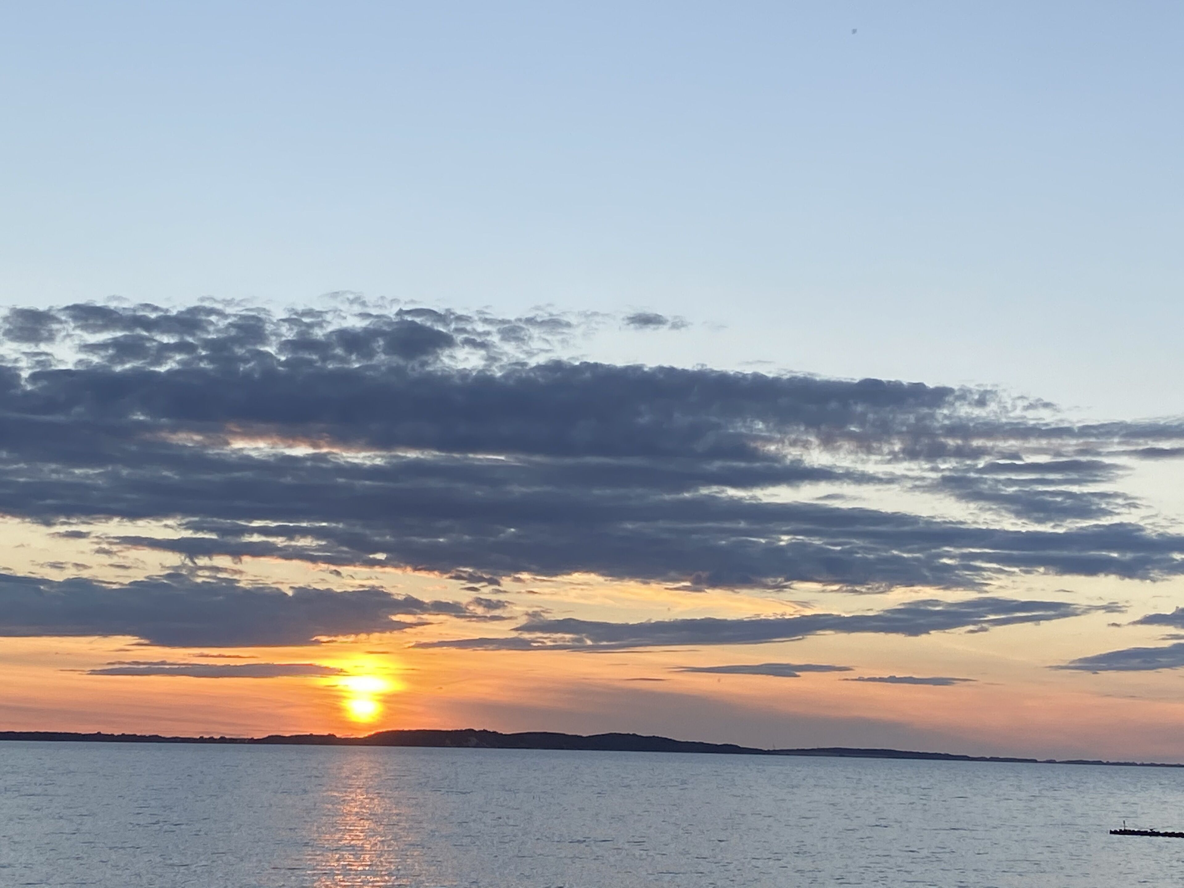 A sunset over a calm body of water with a distant shoreline.