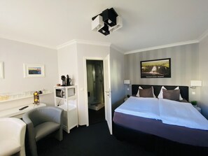 Habitación de hotel con cama, escritorio y silla, zona de ducha y un cuadro en la pared.