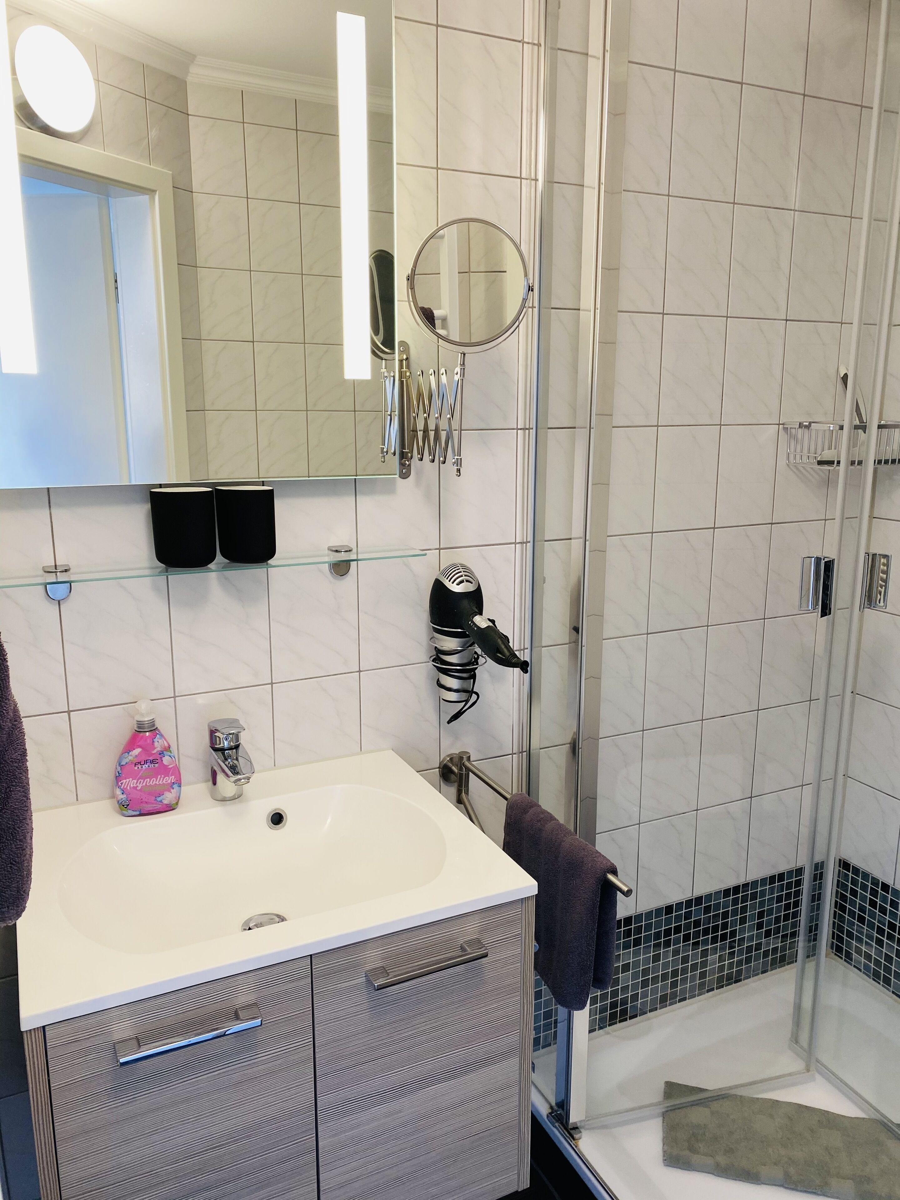 Un bagno moderno con un lavandino bianco, uno specchio e una cabina doccia in vetro.