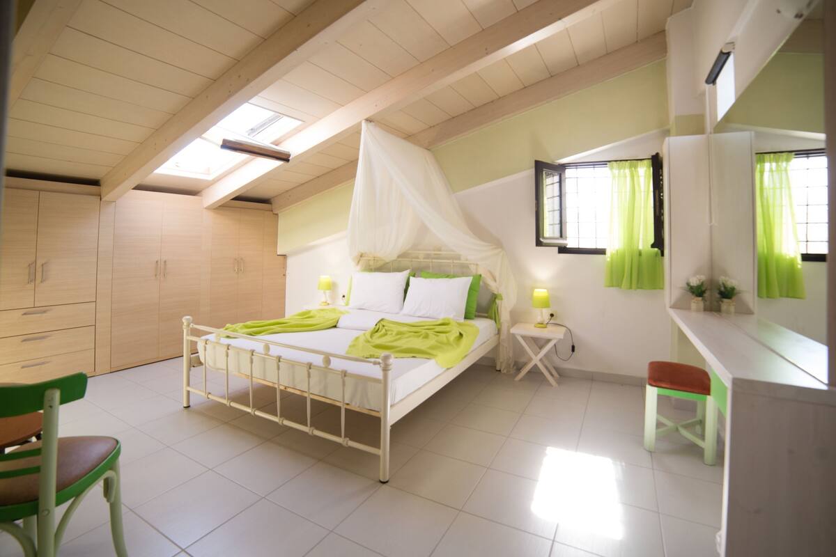 Un dormitorio con cama, una silla, una mesita de noche y una ventana con cortinas.
