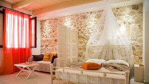 A bedroom with a bed, a nightstand, a chair, a table, and a window with curtains. - AC Homes Christos (Rethymno)