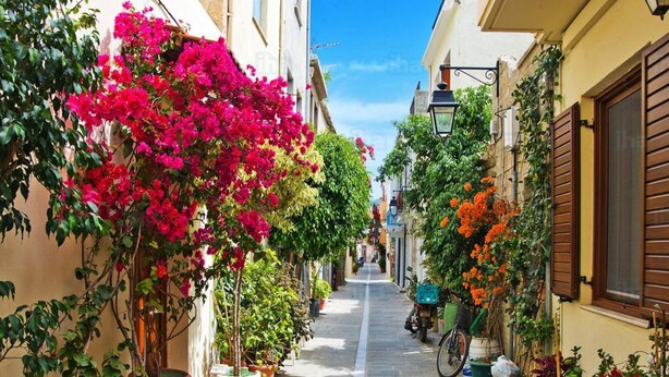 A narrow street lined with buildings, potted plants, and bougainvillea flowers. - AC Homes Christos (Rethymno)