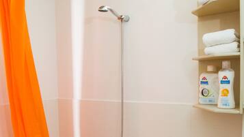 Un baño con bañera, una cortina de ducha naranja, un cabezal de ducha y repisas con artículos de aseo.