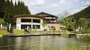 A lakeside hotel with a pool, lounge chairs, and a mountain view. - Landhotel Alpenhof (Filzmoos)