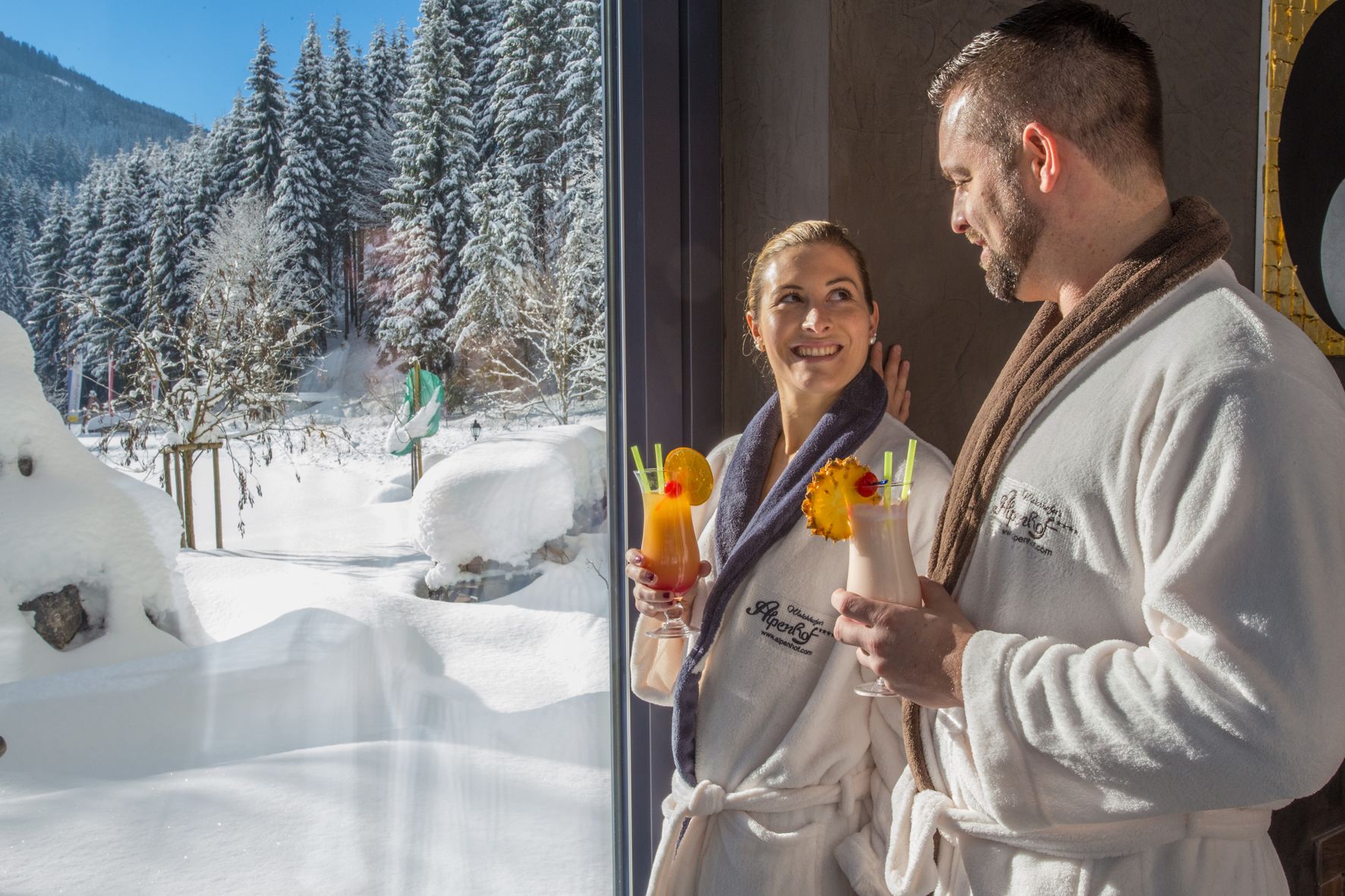 A snowy outdoor scene with a wooden structure and a person in a white robe holding a drink with a straw and a cherry.