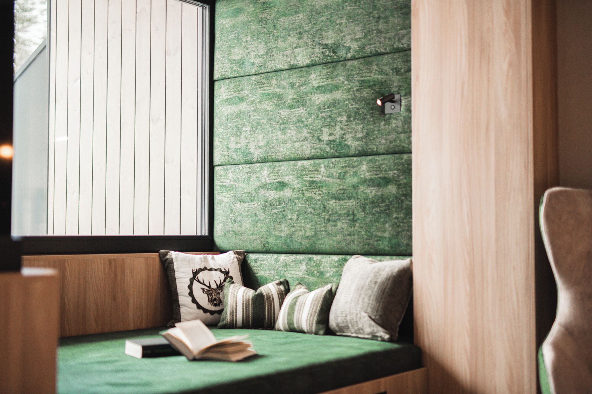 A cozy seating area with a green cushioned bench, a book, and decorative pillows.