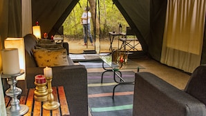 A tented accommodation with a sofa, a table with candles, and a view of the forest.