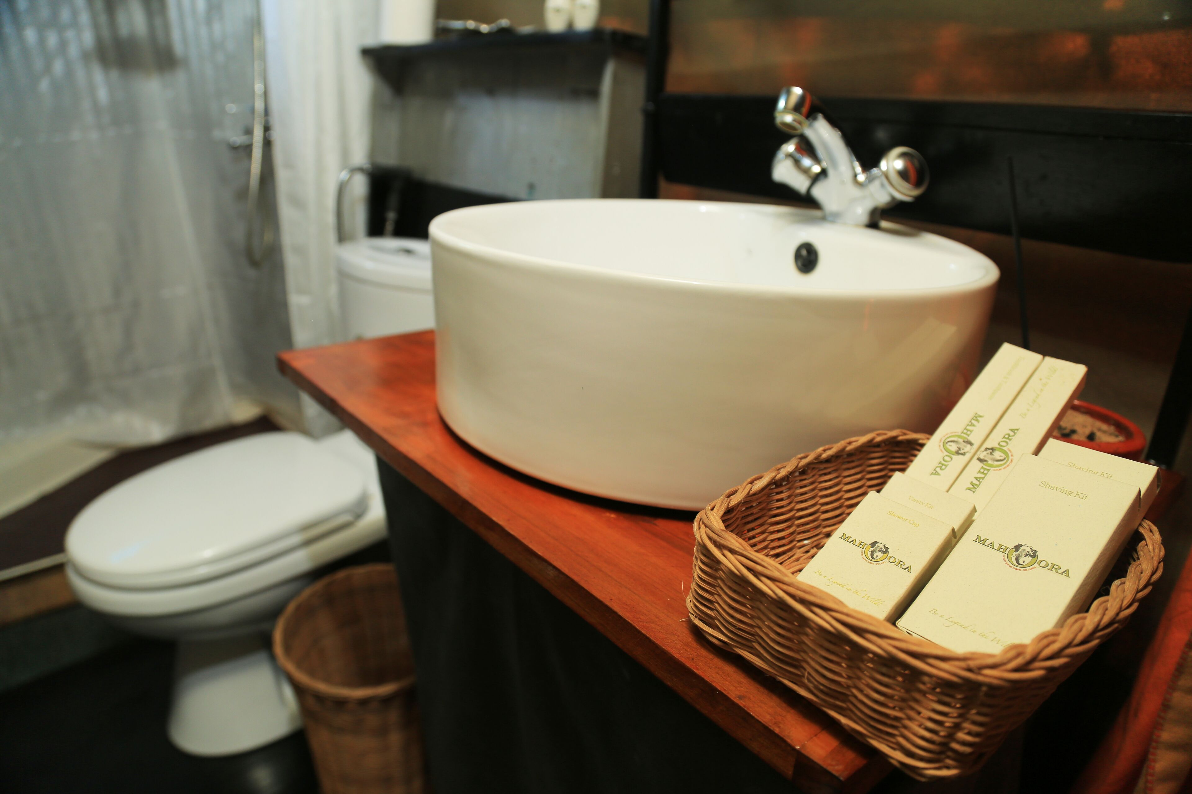 A bathroom with a white sink, a wooden countertop, and a wicker basket containing two boxes of shampoo.