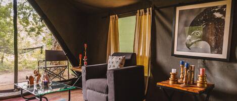 A cozy room with a dark-colored armchair, a glass coffee table, a patterned rug, and a small side table with candles.
