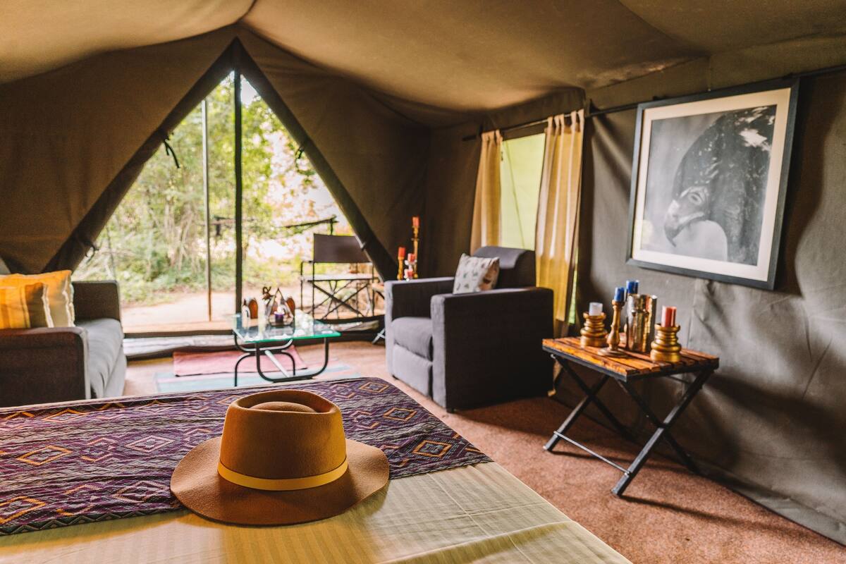 Habitación tipo alojamiento en tienda de campaña, con cama, una mesa con velas, un sofá y un cuadro en la pared.