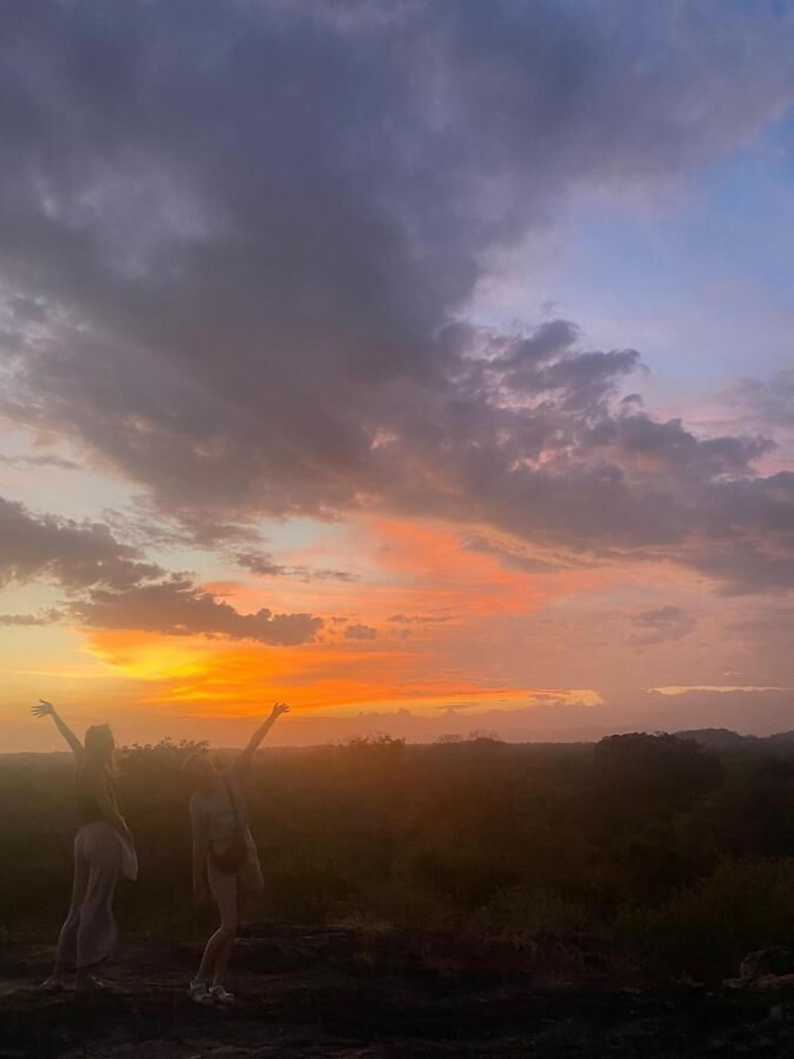A sunset over a hilly landscape with silhouettes of people.