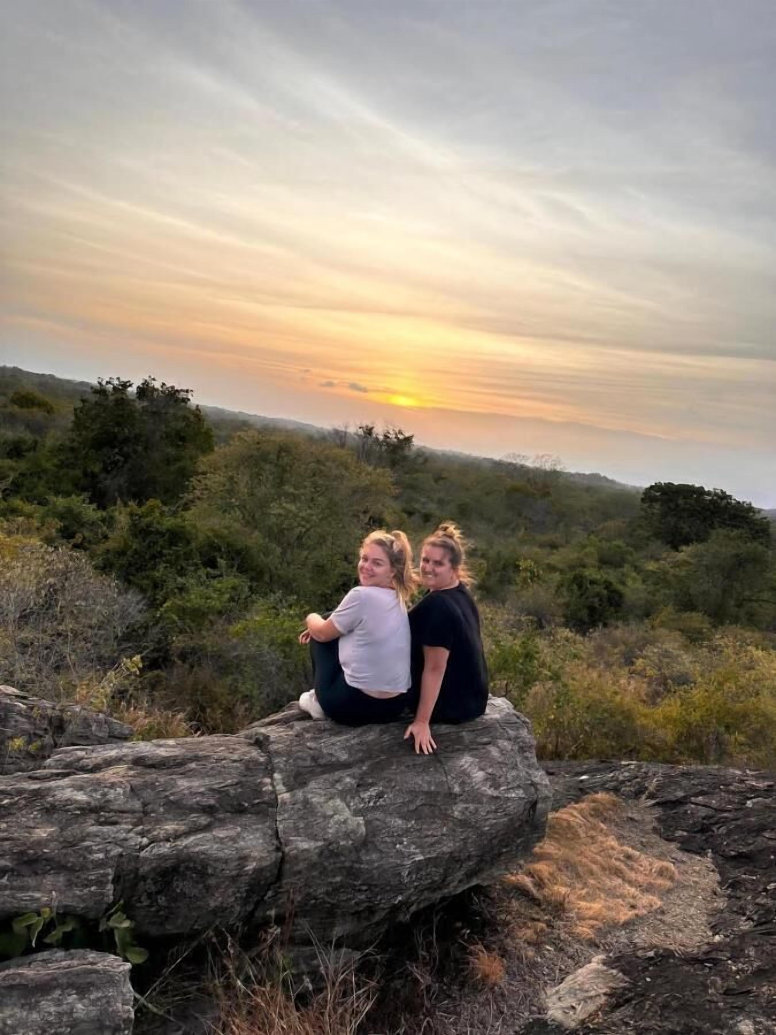 Two people sitting on a rock with a sunset in the background.