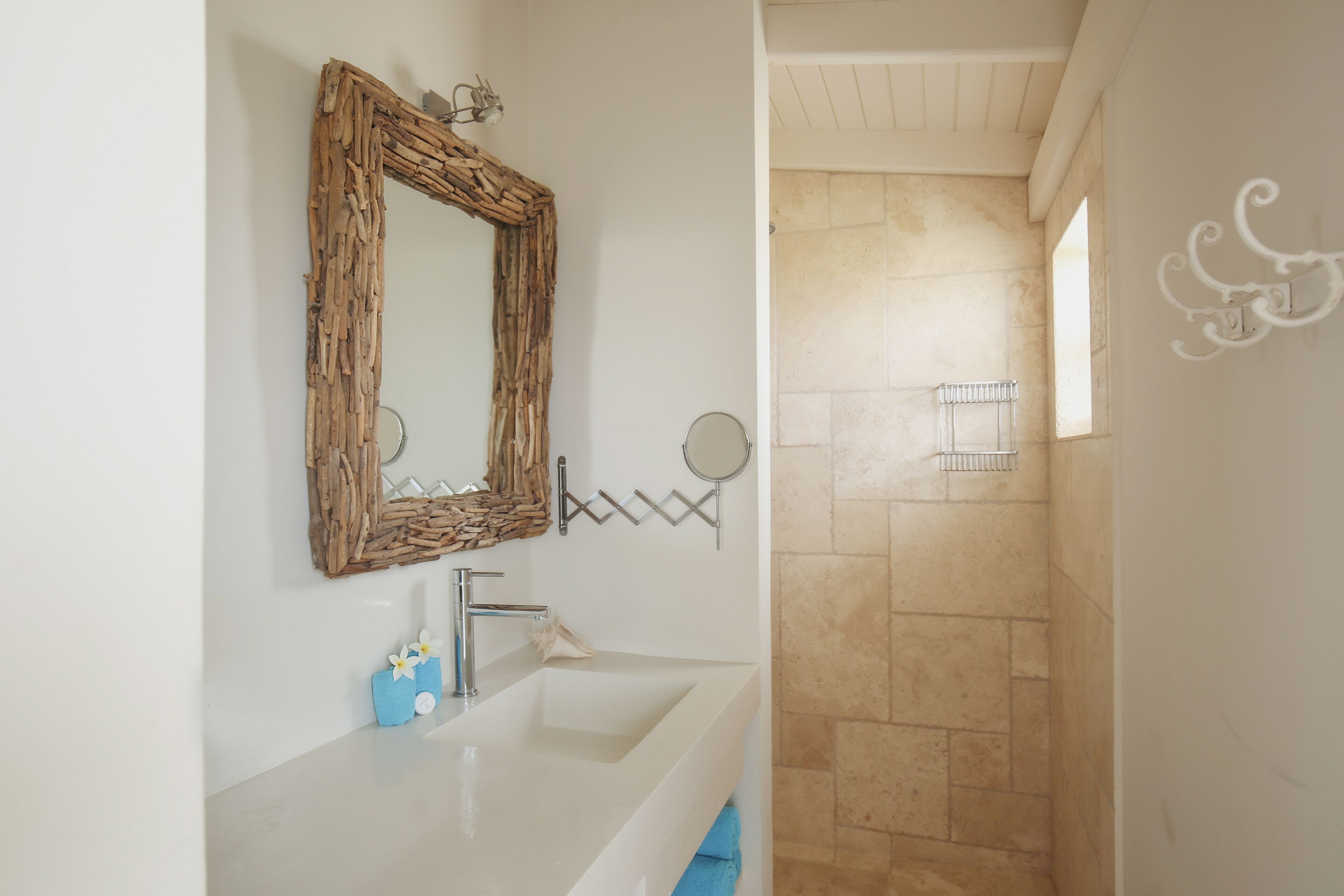 Une salle de bain avec un lavabo blanc, un miroir à cadre en bois et un espace douche aux carreaux beiges.