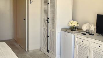 Quarto com cama, guarda-roupa branco, penteadeira e uma pequena mesa com um vaso de flores.