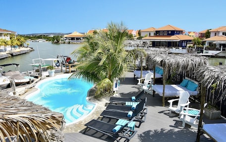A pool area with lounge chairs, a palm tree, and a view of the marina.