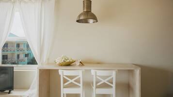 Una habitación con una mesa blanca, dos sillas blancas, una lámpara colgante y una ventana que ofrece vistas a edificios.