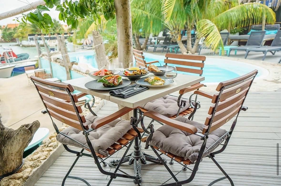 Zona de comedor junto a la piscina con una mesa preparada para cuatro personas, rodeada de sillas acolchadas.