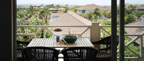 A balcony with a table and chairs, a hanging light fixture, and a view of a residential area with houses and palm trees.