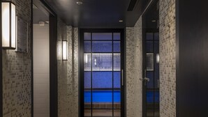 A hallway with mosaic tile walls, a view of a blue pool through a glass door, and a wooden floor.