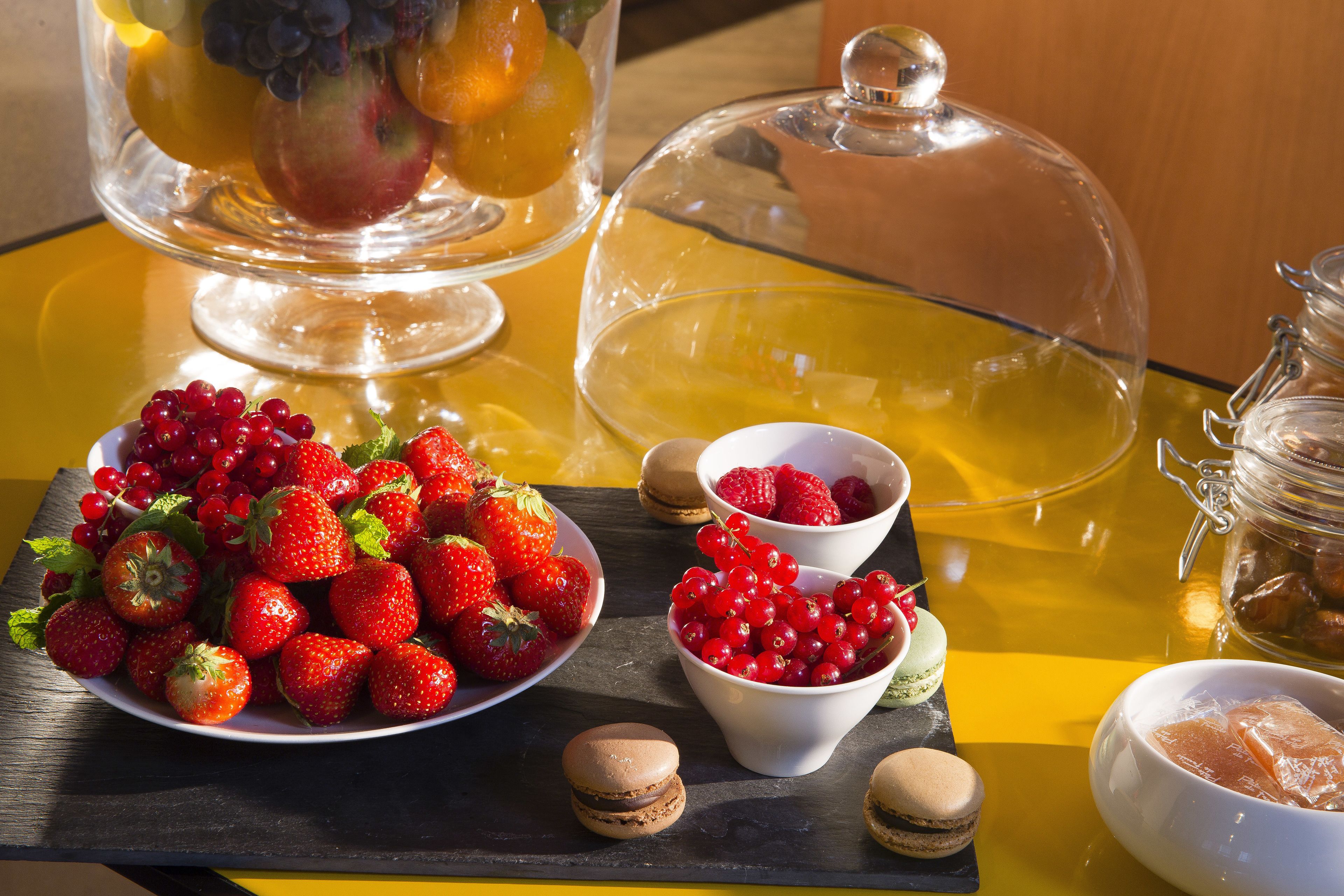 A table with a variety of fruits, including strawberries and red currants, and macarons.