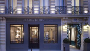 The exterior of Les Martins de Paris Hotel with large windows, a balcony with ornate metal railings, and a Christmas decoration archway.