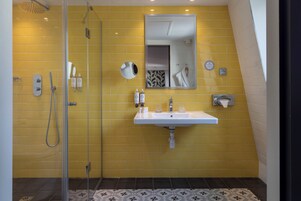 A bathroom with yellow tiled walls, a glass shower enclosure, a white sink, and a mirror above it.