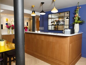 A modern bar area with wooden counter, pendant lighting, and a mirror reflecting the bar.
