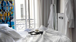 A hotel room with a bed, white pillows, a tray with a cup, and a view of a balcony.